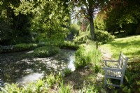 Un banc en bois à côté d'un étang bordé d'iris à l'ancien presbytère, Netherbury, Dorset en mai
