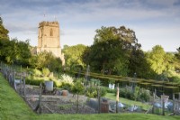 Jardin potager formel sur terrain en pente à l'ancien presbytère, Netherbury, Dorset en mai avec en toile de fond l'église St Mary