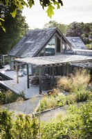 Maison conçue par Hugh Wray-McCann à Am Brook Meadow dans le Devon en juin, où une terrasse en bois le long d'un côté du bâtiment est recouverte d'un toit ouvrant en bois.