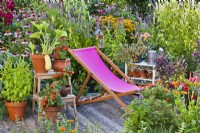 Patio en terrasse avec chaise et pot cultivant des légumes et des herbes bordés d'un parterre de fleurs herbacées avec Agastache et Echinacea.