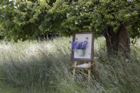 Un vieux chevalet d'artiste et un arrosoir ont été réutilisés pour créer un point focal avec une campanule dans une prairie de fleurs sauvages. Gleam Tor, jardin NGS. Juillet. Été.