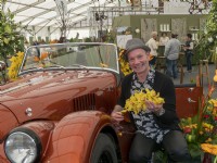 Jonathan Moseley le designer floral à côté d'une voiture Morgan à Malvern et tenant un affichage jaune de fleurs d'orchidées.