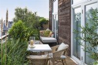 Une salle à manger sur le balcon est bordée de jardinières d'herbes ornementales, d'une baie standard, de pittosporum panaché, d'olivier et de nèfle.