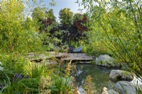 Vue sur l'étang jusqu'au coin salon sur une terrasse en bois en bois. RHS Garden pour un avenir vert. Conçu par Jamie Butterworth. RHS Hampton Court Palace Garden Festival Show, juillet 2021