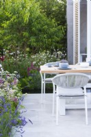 Table et chaises d'extérieur aux couleurs gris froid entourées de parterres de fleurs d'été. Ferme de la grange inférieure : le jardin rebondissant Concepteur : Samuel Moore. RHS Hampton Court Palace Garden Festival Show, juillet 2021.
