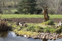 Statue d'oiseau sculpté en bois à côté de l'étang de la faune dans John's Garden à Ashwood Nurseries - Kingswinford - Spring