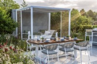 Soleil du matin sur la terrasse avec table à manger et pergola en métal avec sièges en dessous. Ferme de la grange inférieure : le jardin rebondissant, RHS Hampton Court Palace Garden Festival 2021