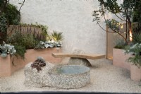 Cour de jardin en pot d'inspiration méditerranéenne avec parterres de fleurs surélevés incurvés, banc en pierre et pièce d'eau.