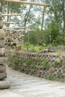 Pots de pavés recyclés et drainage fait de vieilles cuillères en fer. Mur de troncs d'arbres empilés et de tuyaux de drainage en béton.