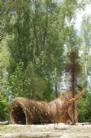 Arche de branches de saule et statue humaine en acier corten comme landart conçu par Will Beckers.
