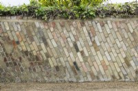 Style inhabituel de maçonnerie dans un vieux mur de jardin avec des briques récupérées posées à un angle. Courses verticales obliques.