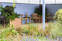Jardin avec coin salon couvert à côté d'un étang planté d'Iris 'White Swirl', Hostas, Carex buchananii et Nepeta 'Summer Magic' reflétant la couleur bleue des murs - SSAFA Sanctuary Garden. Créatrice : Amanda Waring