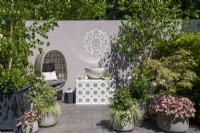 Chaise en rotin à côté d'une pièce d'eau sur un support carrelé entouré de plantes en pots - The Mandala Garden, RHS Chelsea Flower Show 2022 - Médaille d'argent