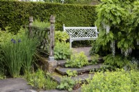 Un banc de jardin en bois orné dans le jardin inférieur Rill à Wollerton Old Hall Garden, avec Iris siberica, et Alchemilla mollis, Ladies Mantle.