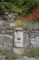 Tête sculpturale de style île de Pâques plantée d'une herbe ornementale pour ajouter de l'intérêt au terrassement. Le printemps