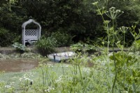 Une vue sur un étang à une tonnelle en bois siège et bateau à rames en bois. Lewis Cottage, jardin NGS Devon. Le printemps.