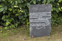 Une ardoise recyclée porte une citation sur le jardinage et est affichée à côté d'une haie de hêtres. Lewis Cottage, jardin NGS Devon. Le printemps
