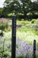 Poteaux en bois noir avec les noms de femmes jardinières renommées utilisées pour identifier les zones de culture dans une ferme florale en juillet