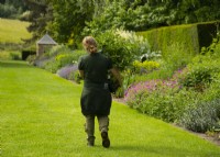 Un jardinier transportant une grande plante dans un pot le long de la pelouse entre les parterres doubles à Newby Hall.