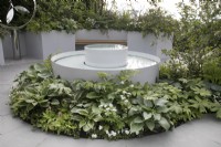 Dispositif d'eau circulaire entouré de plantations vertes et blanches et de pavage circulaire dans le jardin CRUK Legacy au Malvern Spring Gardening Festival 2022