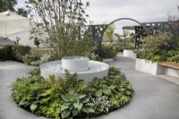Dispositif d'eau circulaire entouré de plantations vertes et blanches et de pavage circulaire dans le jardin CRUK Legacy au Malvern Spring Gardening Festival 2022