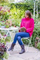 Femme assise à une table lisant sur un patio entouré de plantes