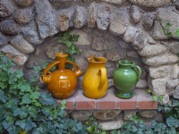 Des cruches de vin en poterie décorent une alcôve dans un mur de jardin en pierre