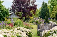 Le Cottage Garden vue sur des parterres de fleurs avec des sièges en pierre, juillet 2022.