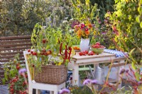 Bouquet de fleurs sur table et légumes en pot sur terrasse aménagée avec salon de jardin.