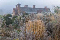 Topiaire d'if et plantes vivaces et graminées ornementales couvertes devant dans un jardin de campagne formel en hiver - janvier