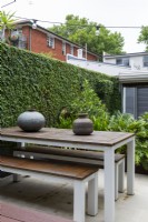 Deux pots décoratifs sur une table en métal et en bois avec banquettes dans un jardin de la cour.