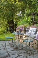 Terrasse en dallage en pierre avec mobilier de jardin en métal et composition florale.