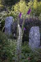 Parterres de fleurs de jardin profonds de style cottage parsemés de pierres dressées en granit et de fougères en acier galvanisé par un artisan de Cornouailles 'Steeling nature'