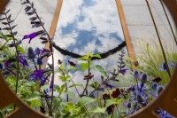 Vue à travers le panneau en acier Corten jusqu'à la plantation de Salvia 'Amistad', Eryngium et reflets dans la piscine - The Sunburst Garden, RHS Hampton Court Palace Garden Festival 2022