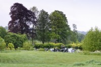 Jardin de campagne avec pente herbeuse menant à un lac en mai