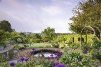 Jardin de roses en terrasse formel avec étang circulaire et beaucoup d'Allium 'Purple Sensation' en mai.