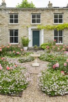 Rosa 'Summer Beauty' syn. Rosa 'Korobe' et Geranium x cantabrigiense 'St Ola' plantés dans des plates-bandes circulaires devant un studio de jardin en briques à l'échelle 2/3 conçu pour ressembler à une maison. Peut