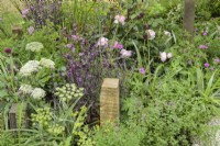 Plantation mixte de vivaces parmi des poteaux en bois dans A Journey, en collaboration avec Sue Ryder garden au RHS Hampton Court Palace Garden Festival 2022