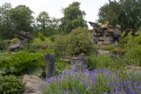 Géraniums et Gunnera manicata autour d'une sculpture en métal et de formations rocheuses à Paxton's Rock Garden, Chatsworth House and Garden.