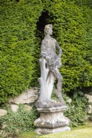 Figure sculptée patinée de l'homme à côté d'un muret et d'une haie d'ifs.