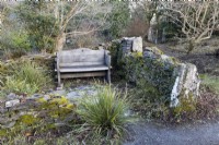 Un banc en bois niché dans l'angle d'un mur en pierres sèches. La maison du jardin, Yelverton, Devon