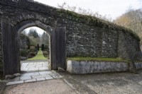 Une ancienne arche, avec de grandes portes en bois, dans un haut mur de briques, mène au jardin clos. La maison du jardin, Yelverton, Devon