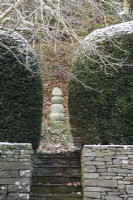 Point focal de pierres empilées encadrées de haies d'ifs dans un jardin en décembre.