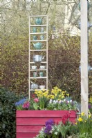 Pots en bois peints en violet remplis de jacinthes, de muscari, de tulipes et de jonquilles devant la décoration avec des bouilloires et des tasses à thé.