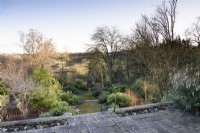 Le Step Garden plein d'arbustes d'intérêt hivernal avec pavillon en bas à Cotswold Farm Gardens en février.
