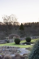 La terrasse Jewson à Cotswold Farm Gardens en février avec des parterres de fleurs géométriques et des conifères taillés, y compris des ifs et des buis.