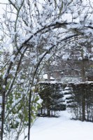 Vue à travers l'arche de rose couverte de neige dans un jardin de ville formel. Décembre