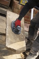 Un ouvrier utilisant un élévateur à vide pour soulever une dalle de York Stone pour une terrasse en pierre lors de la rénovation d'un petit jardin londonien.