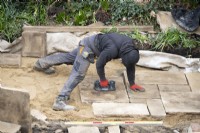 Un ouvrier utilisant un élévateur à vide pour poser des dalles de York Stone pour une terrasse lors de la rénovation d'un jardin londonien.