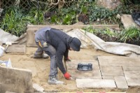 Un ouvrier pose des dalles de York Stone pour une terrasse lors de la rénovation d'un petit jardin londonien.